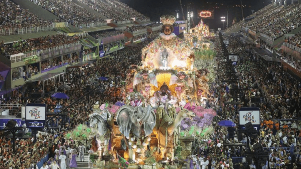 Spectacular view of a samba school parade at Carnaval, featuring an elaborate float with intricate designs, costumes, and a large crowd in the background.