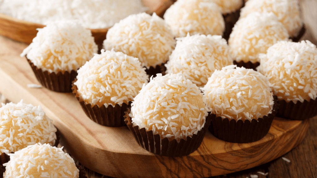 A close-up of beijinhos, Brazilian coconut truffle balls, coated in granulated sugar with a single clove stuck in the top of each, arranged on a wooden board.