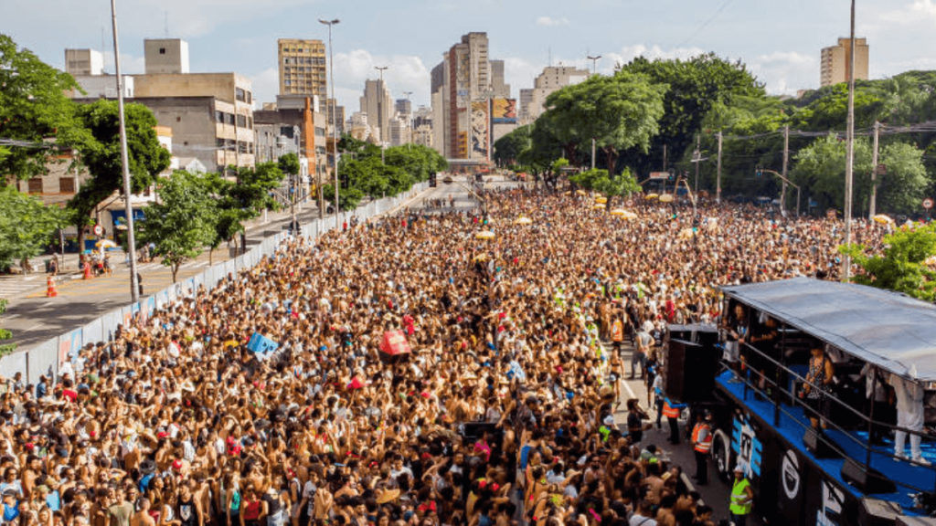 Thousands of people celebrating in the streets at a São Paulo carnival block, with a festive truck in the background.