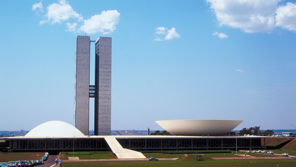 A daytime view of the National Congress of Brazil in Brasília, featuring the distinctive twin towers and the dome of the Senate.