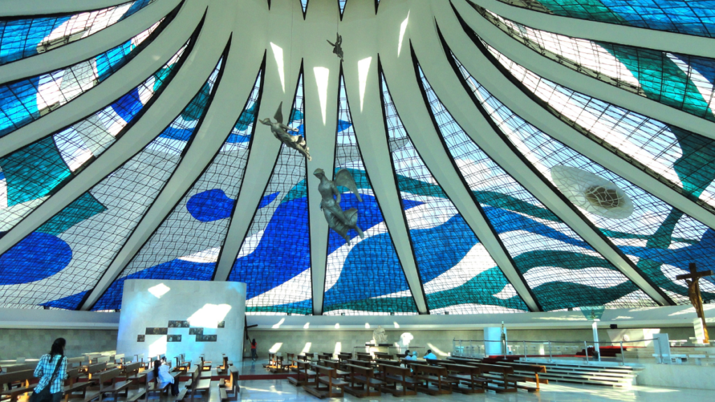 Interior view of the Cathedral of Brasília, showing the intricate blue and white stained glass and the angel sculptures suspended from the ceiling.