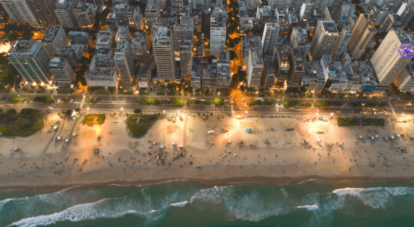 An aerial nighttime view of Ipanema Beach, illuminated by city lights that reveal the urban grid pattern and the sandy shores of one of Brazil's most renowned beaches.