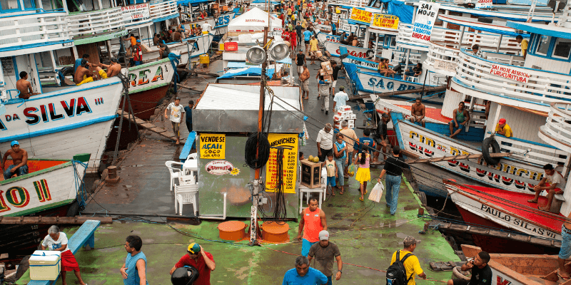A bustling port in Manaus with colorful boats docked along the pier, vendors selling goods, and a crowd of locals and travelers navigating the busy marketplace.