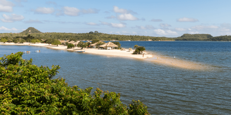 A tranquil beach in Alter do Chão near Santarém, with clear waters gently lapping against a sandy spit, surrounded by lush greenery and a clear blue sky.