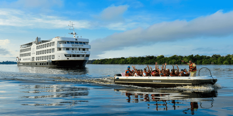 A riverboat cruise on the Amazon River with a large cruise ship in the background and a smaller boat carrying tourists in the foreground, showcasing eco-tourism in Brazil's vast river system.