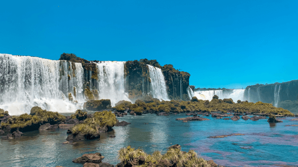 Crystal clear blue skies over Iguazu Falls, with cascading waters flowing amidst verdant islets and rocks.