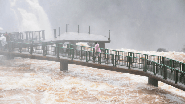  flooded walkway at Iguazu Falls, with turbulent golden-brown waters suggesting the raw power of nature during high flow