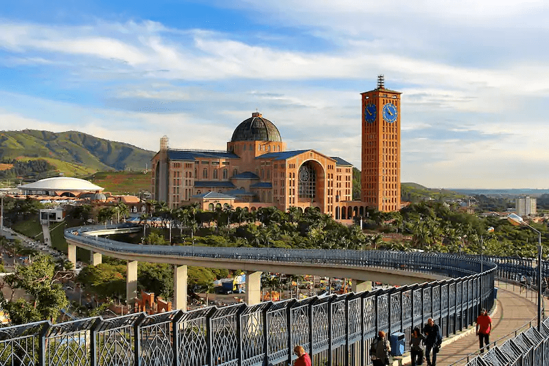 The grand Basilica of the National Shrine of Our Lady of Aparecida, the large Catholic church with a distinctive blue dome and tower, set against a scenic landscape, the bigest temple of religion in Brazil.