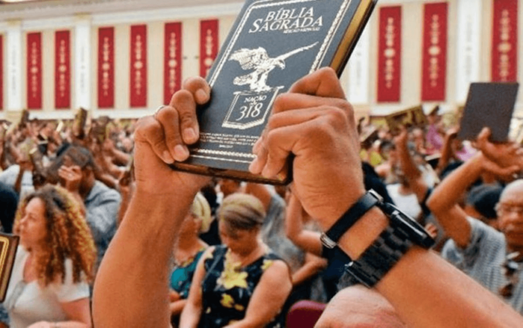 A congregation of people raising their Bibles during a religious service, with a focus on a Bible titled "Bíblia Sagrada," symbolizing a Protestant Christian gathering in Brazil, one of the main religion ib Brazil.