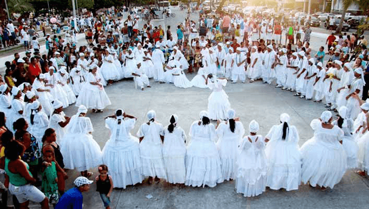 An outdoor gathering of Candomblé practitioners dressed in white, performing a ritual dance in a circle, showcasing the communal aspect of the religion in Brazil.