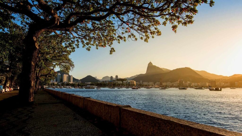 A peaceful sunset view of Mureta da Urca in Rio de Janeiro, with the bay and Sugarloaf Mountain in the background, creating a serene atmosphere. A perfect spot to enjoy a drink with locals.