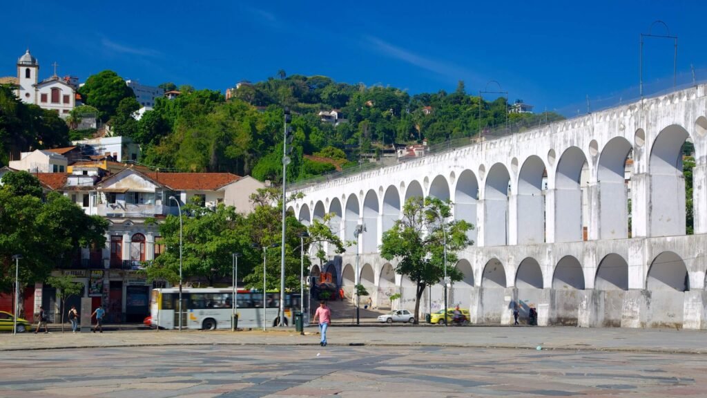 The famous Lapa Arches in Rio de Janeiro, a historic aqueduct standing tall with vibrant greenery in the background and people walking nearby. A must-visit for exploring Rio’s vibrant culture.