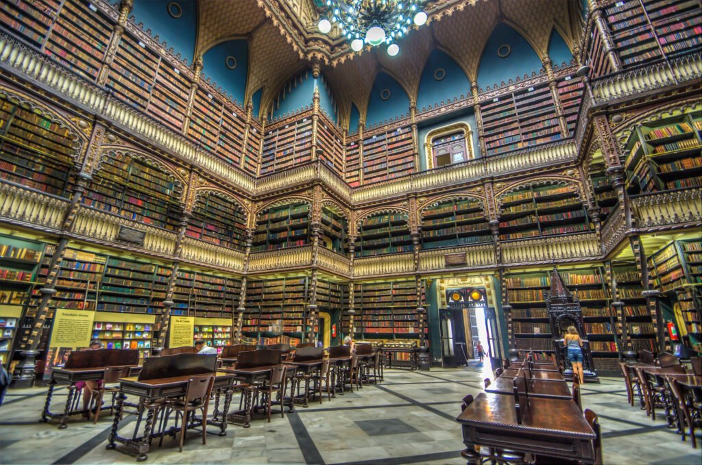 The stunning interior of the Real Gabinete Português de Leitura in Rio de Janeiro, showcasing towering bookshelves filled with thousands of historic books and ornate Gothic architecture, bathed in warm light.